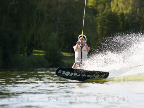 Sporty young man with helmet and waistcoat on wakeboard in lake, water sports, water skiing in wakepark