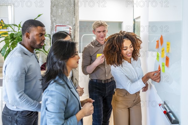 Diverse team collaborating, using sticky notes on a whiteboard during a brainstorming session in a modern coworking office