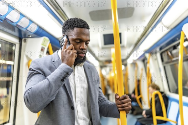 Young businessman having phone call while commuting on subway train, holding onto handrail