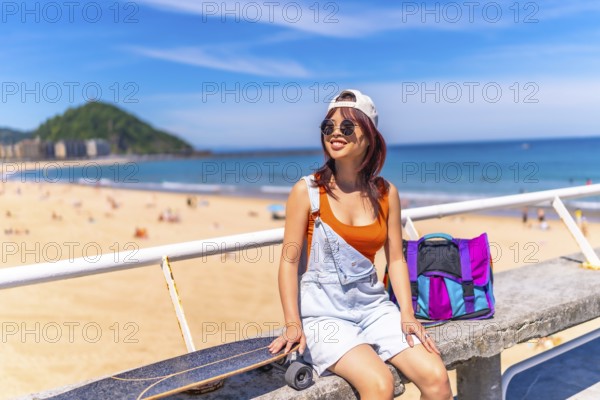 Horizontal photo with copy space of an asian young woman sitting on a promenade with skateboard in summer