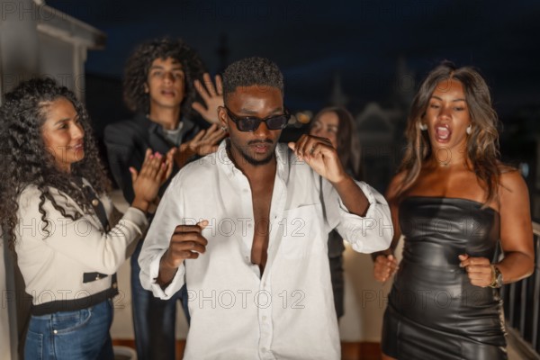Brunette cool man in sunglasses dancing surrounded by friends at night in a city roof