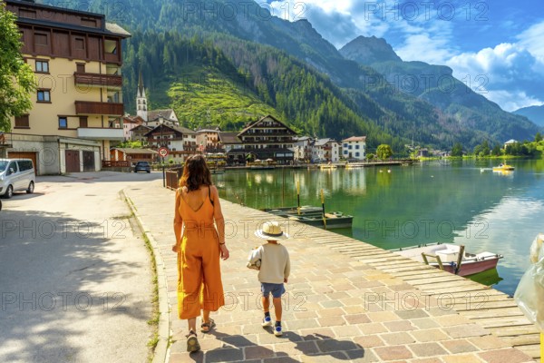 Mother and son walking on a paved pathway by the alleghe lake in the italian dolomites, enjoying summer holidays
