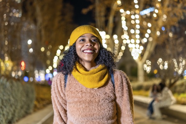 Portrait of a young woman wearing winter clothes, enjoying christmas lights in a decorated city at night