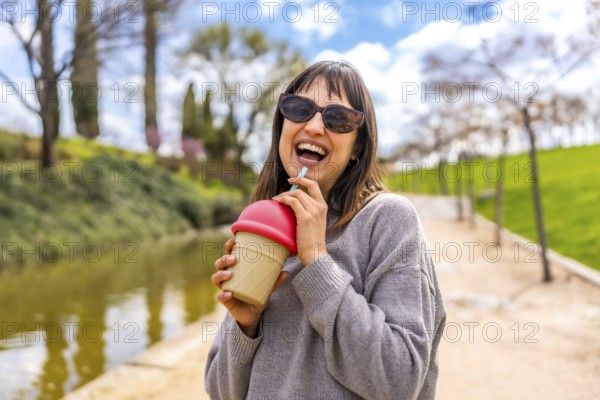 Carefree young woman enjoying a refreshing drink on a sunny day in a park, embodying a sense of joy and relaxation