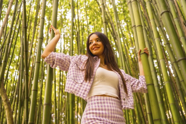 Young caucasian girl with a pink skirt in a bamboo forest. Enjoying summer holidays in a tropical climate, walking in the forest grabbing the trunks of bamboo and smiling