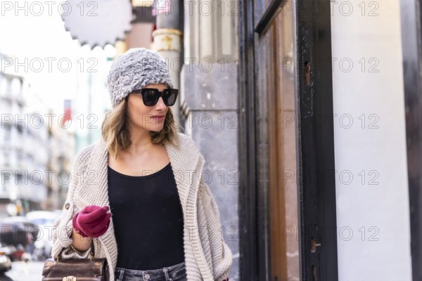 Lifestyle, young Caucasian blonde girl enjoying and smiling in the city in winter. Strolling with sunglasses and red gloves