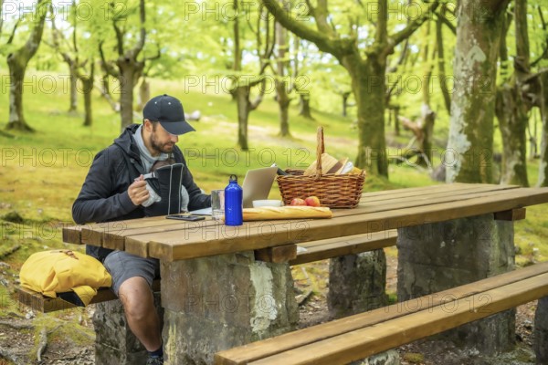 A young Caucasian father teleworking sitting at a picnic table with computer in the woods. Summer lifestyle