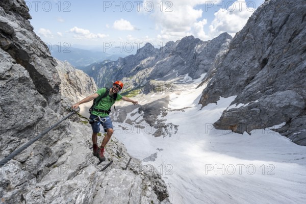 Mountaineer with helmet in a secured via ferrata, Zugspitze via ferrata, ascent to the Zugspitze, view of mountain basin with snow field of the Höllentalferner and Höllental, Wetterstein range, Bavaria, Germany, Europe