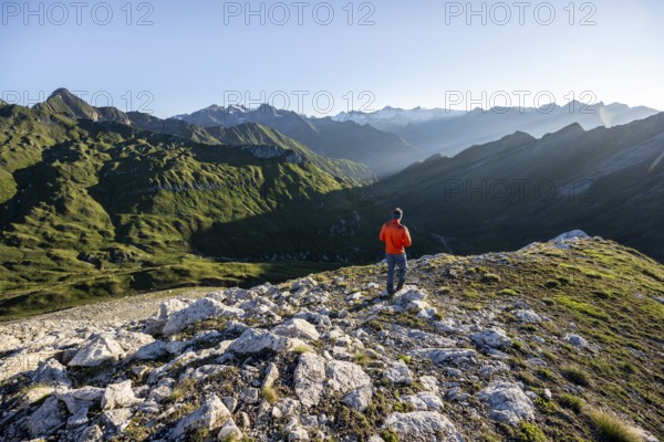 Mountaineer in front of mountain landscape at sunrise, view of mountain peaks of the Venediger group and into the Großbachtal valley from the summit of Bachlenkenkopf, Lasörling group, Hohe Tauern National Park, East Tyrol, Tyrol, Austria, Europe