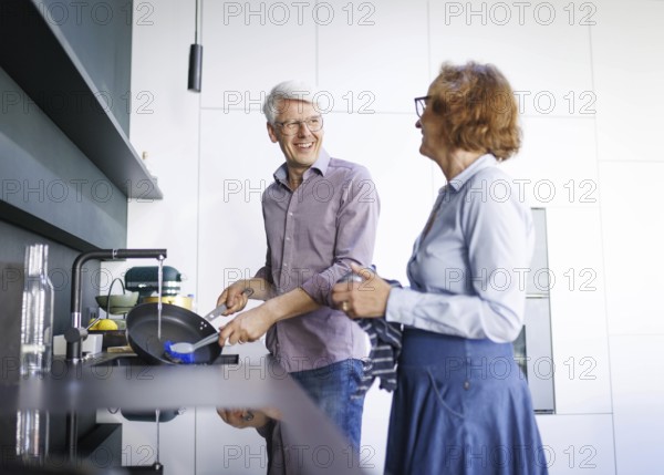 Symbolic photo. An elderly couple stand in the kitchen and do the washing up together. Berlin, 13.08.2024