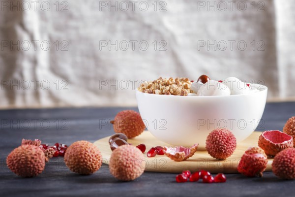 Greek yogurt with lychee, pomegranate seeds and granola in a white plate on a black wooden background, close up