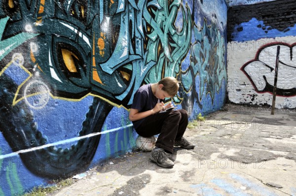 Ten-year-old boy playing with his Nintendo in front of a graffiti wall, football pitch, Germany, Europe