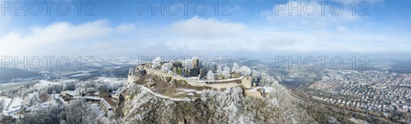 Aerial panorama of the snow-covered Hegau volcano Hohentwiel with Germany's largest castle ruins, surrounded by frosty trees in a winter landscape, on the right the town of Singen, district of Constance, Baden-Württemberg, Germany, Europe