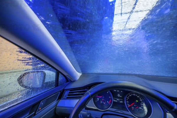Car in an automatic car wash, car wash tunnel, cleaning foam is sprayed on, rotating brushes clean the vehicle