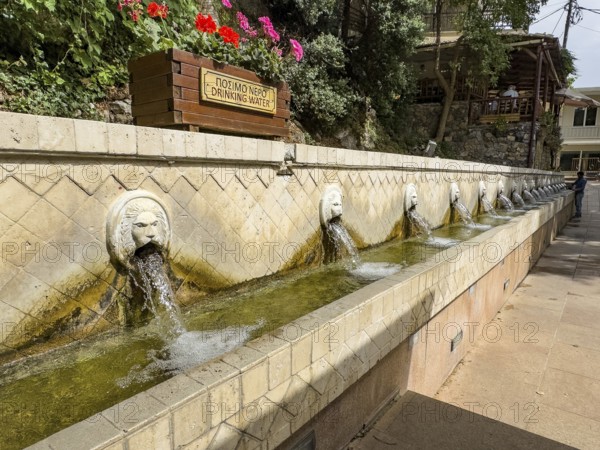 Partial view of lion fountain Venetian fountain Kefalovrisi with 25 waterspouts in the shape of lion's head Lion's head above Plla chain sign Drinking water Drinking water below Catch basin with drinking water on main square of village Spili, Spili, Crete, Greece, Europe
