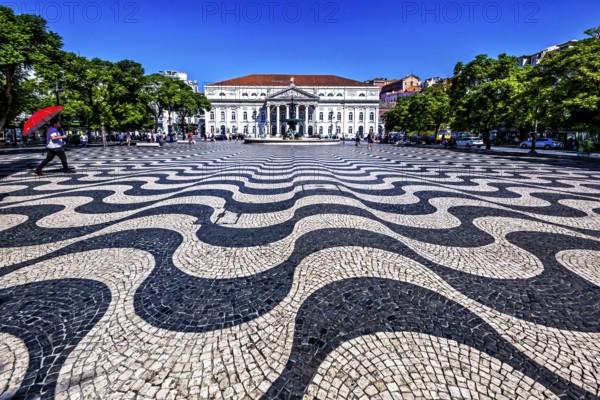 Wavy black and white patterned pavement in a sunny urban square with people and classic building in background, Lisbon