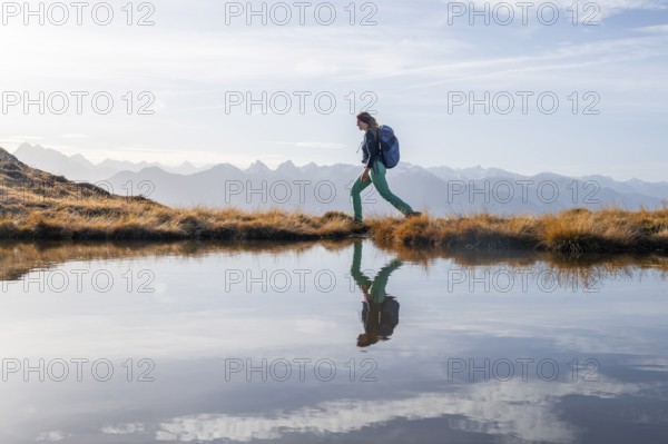 Hiker reflected in a small mountain lake on the Krahberg, mountain panorama in autumn, Venet crossing, Ötztal Alps, Tyrol, Austria, Europe