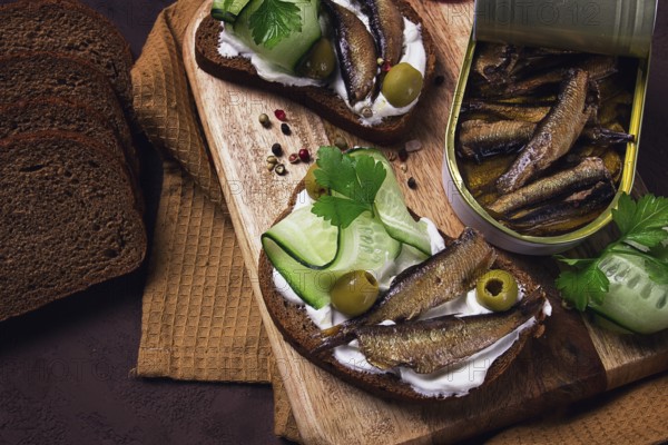 Sandwiches, black bread with sprats, cream cheese, cucumbers, on a cutting board, top view, close-up, no people