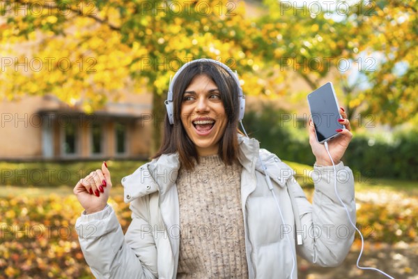 Frontal view of a cute beauty caucasian woman listening to music and dancing in a park enjoying autumn
