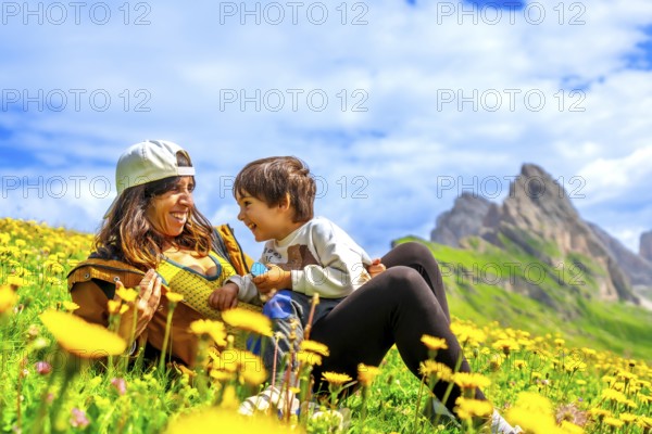 Mother and son relaxing in a dandelion field, enjoying the breathtaking view of the seceda mountains in the dolomites, italy