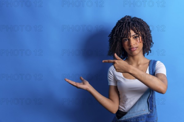 Young woman pointing her finger to the side and showing something with her open hand on a vibrant blue background