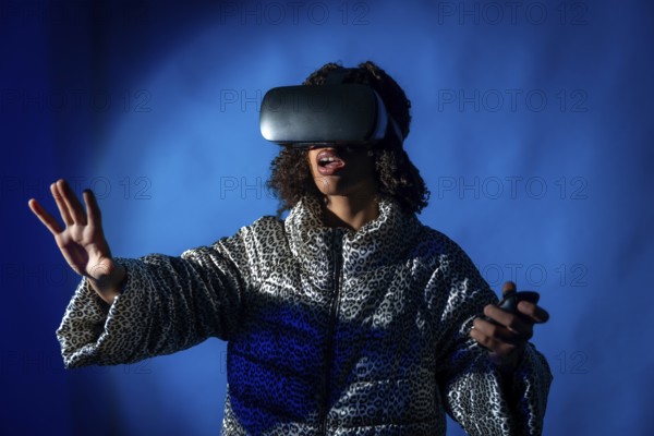 Young woman wearing a vr headset and holding controllers, expressing surprise while immersing in virtual reality against a blue background