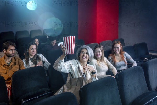 Mature woman enjoying a film in a movie theater, holding a popcorn bucket, surrounded by other people