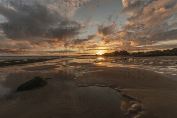 A beach with a rock and a sunset, the sky is reflected on the sand of a beach. The sky is cloudy and the sun is out. Les Sables d'Olonne, Vendee, France, Europe