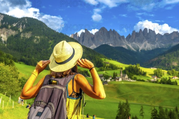 Female tourist holding her hat while admiring the stunning view of the odle mountains and santa maddalena church in val di funes