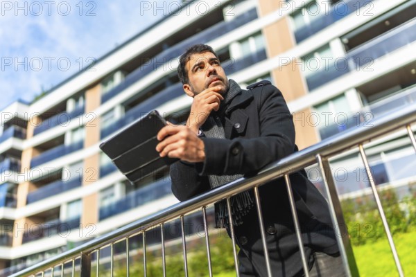 Low angle view potrait of a caucasian pensive businessman in casual winter clothes using digital tablet standing in the city
