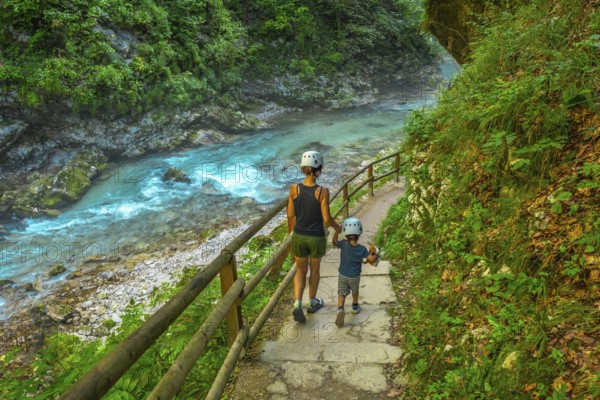 Tourists wearing helmets are enjoying a summer walk along the stunning turquoise radovna river flowing through the vintgar gorge near bled, slovenia