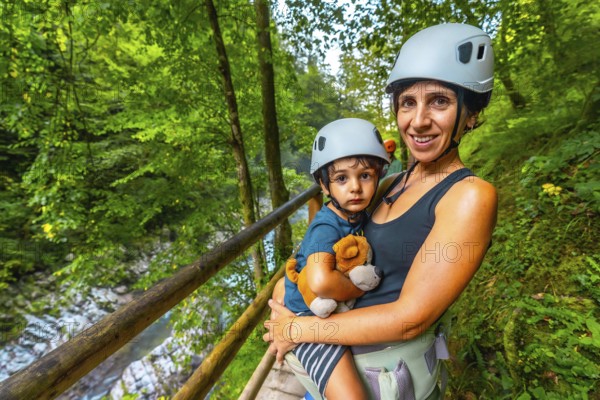 Mother holding her son while wearing helmets and enjoying the stunning view of vintgar gorge near bled, slovenia, creating cherished family memories