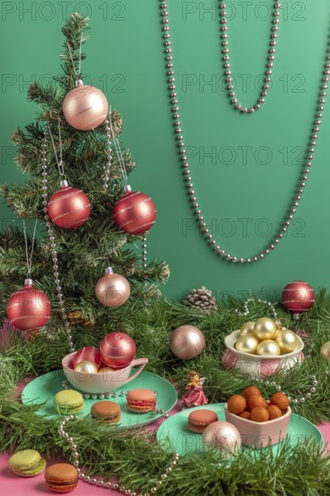 Table scene with small Christmas tree, pink baubles and macaroons, surrounded by green branches
