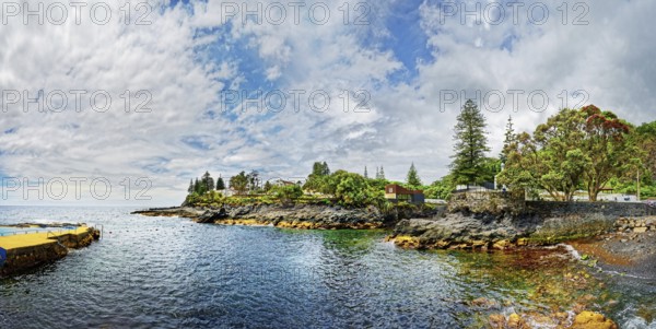 Coastal landscape with houses and trees under a serene sky, the calm sea surrounds the rocky coast, fishing village Caloura, Ribeira Chã, Sao Miguel Island, Azores, Portugal, Europe