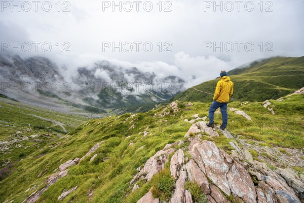 Mountaineer with yellow jacket looking at mountain landscape, cloudy rocky mountain peaks Wolayer Köpf and Biegenköpfe, Carnic Alps, Carnic High Trail, Carinthia, Austria, Europe