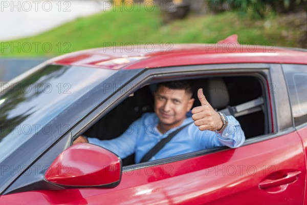 Smiling driver in his car giving a thumbs up. Male driver showing thumbs up while driving