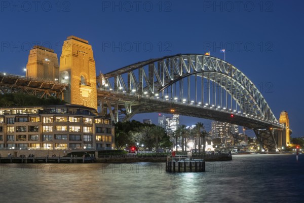 Sydney Harbour Bridge at night, illuminated at blue hour, with city lights in the background and reflecting water in the foreground, Sydney, Australia, Oceania
