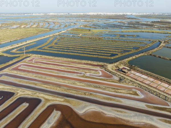 Saline ponds at the salt works near Chiclana de la Frontera. The orange-red colour depends on the level of salinity and is directly caused by the algae Dunaliella salina and brine shrimp. Aerial view. Drone shot. Bahía de Cádiz Nature Reserve, Cádiz province, Andalusia, Spain, Europe
