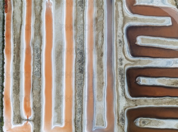Saline ponds at the salt works near Chiclana de la Frontera. The orange-red colour depends on the level of salinity and is directly caused by the algae Dunaliella salina and brine shrimp. Aerial view. Drone shot. Cádiz province, Andalusia, Spain, Europe