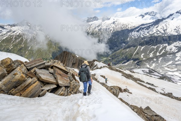 Mountaineer on a rocky ridge with snow, descent from the summit of Schönbichler Horn, view of snow-covered mountain peaks and valley Zemmgrund, Berliner Höhenweg, Zillertal Alps, Tyrol, Austria, Europe