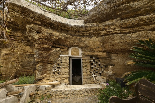Exterior view of a cave carved into the rock with a stone wall and vegetation around the entrance, Agios Nikolaos rock church, Oasis Beach, Kallithea, Rhodes, Dodecanese, Greek Islands, Greece, Europe