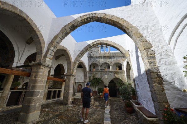 Historic monastery courtyard with stone arcades and bright white walls. Tourists explore the architectural beauty, Inside the monastery, Agiou Theologou Monastery, Chora, Patmos, Dodecanese, Greek Islands, Greece, Europe