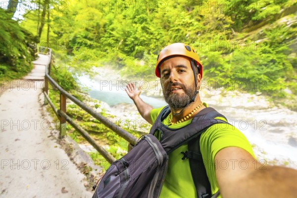 Tourist wearing an orange helmet and backpack takes a selfie while visiting vintgar gorge near bled in slovenia