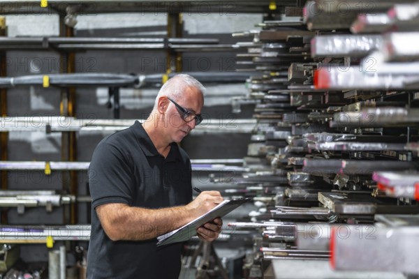 Side view photo of a mature caucasian man checking metal bars while doing inventory using a clipboard in a factory