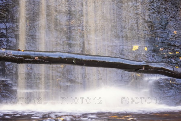 Waterfall on a rock face with a tree log