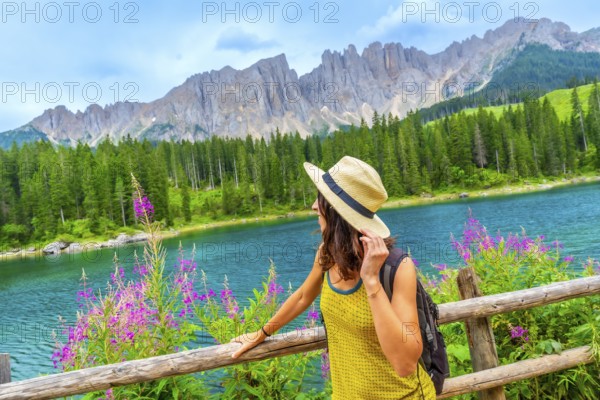 Woman enjoying the landscape of lake carezza with the latemar mountain range in the background, dolomites, italy