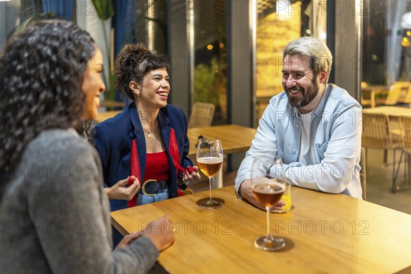 Multiracial friends enjoying night talking and drinking beer and cocktail in a bar terrace