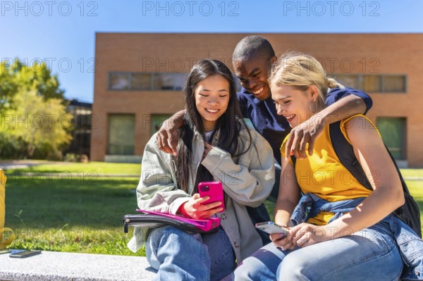 Happy multi-ethnic students using mobile and sitting outside the university campus in a sunny day