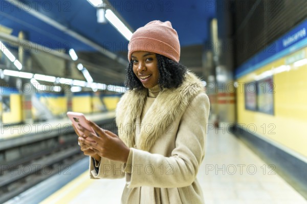 Stylish young woman using mobile phone while waiting for subway train, enjoying her commute in modern urban environment