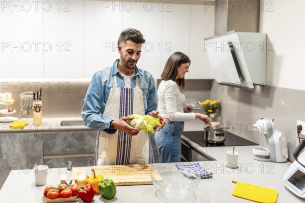 Man holding lettuce and woman cooking in a modern kitchen, preparing a healthy meal together